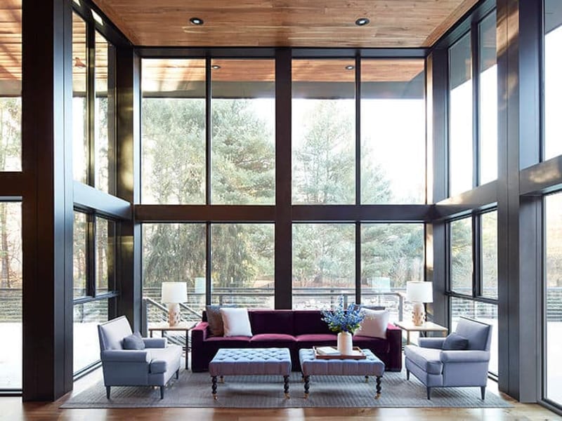 A floor-to-ceiling black-framed window wall wrapping a living room under a timber ceiling